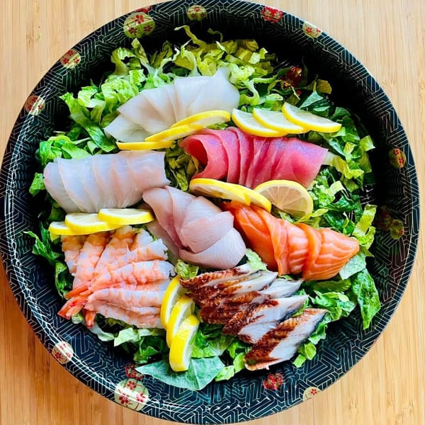 Awi Sushi's sashimi salad with various fish, shrimp, and eel over lettuce with lemon slices.