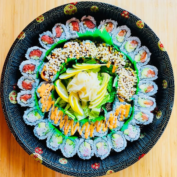 A large, round Awi Sushi platter filled with various sushi rolls, ginger, and lemon slices.