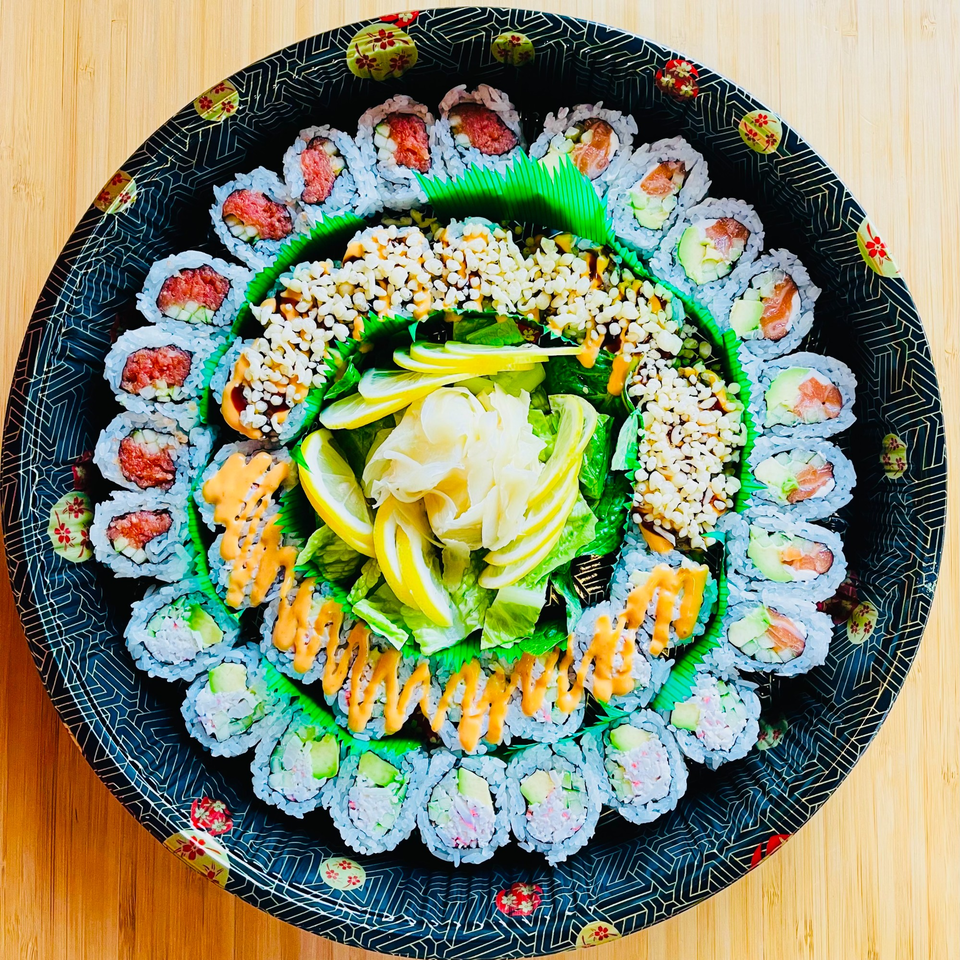 A large, round Awi Sushi platter filled with various sushi rolls, ginger, and lemon slices.