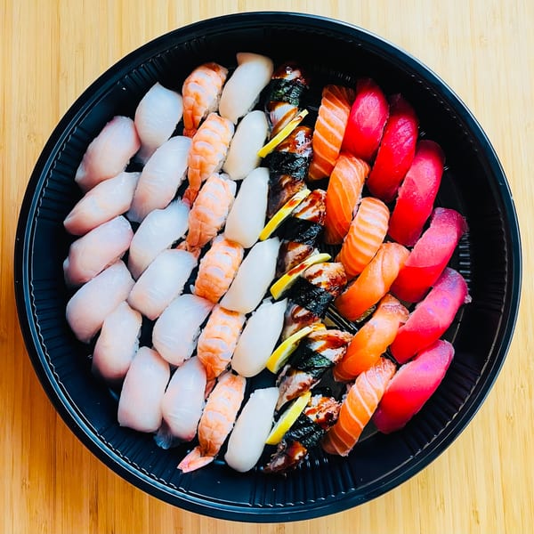 A large black platter of Awi Sushi nigiri, including salmon, tuna, shrimp, and white fish.