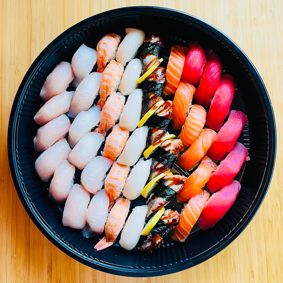 A large black platter of Awi Sushi nigiri, including salmon, tuna, shrimp, and white fish.