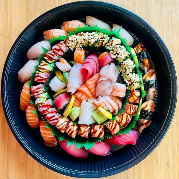 A large black platter of Awi Sushi's assorted sushi and sashimi, including rolls, nigiri, and sliced fish.