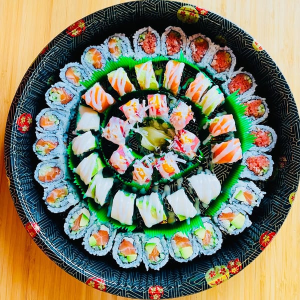 A large, round black platter filled with various Awi Sushi rolls and sashimi on a wooden table.