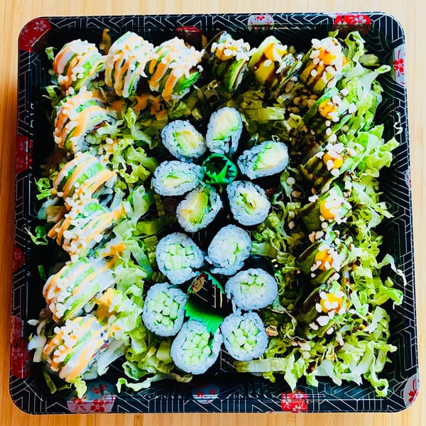 Awi Sushi platter with various sushi rolls, including avocado, cucumber, and drizzled sauces, on lettuce.