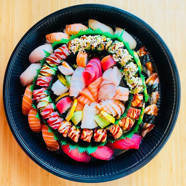 A large black platter of Awi Sushi's assorted sushi and sashimi, including rolls, nigiri, and sashimi.