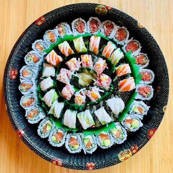 A large, round sushi platter from Awi Sushi with various rolls, sashimi, and ginger on a wooden table.