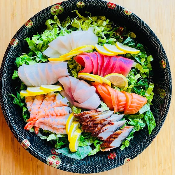 A colorful Awi Sushi sashimi salad with various seafood, lettuce, and lemon slices in a black bowl.