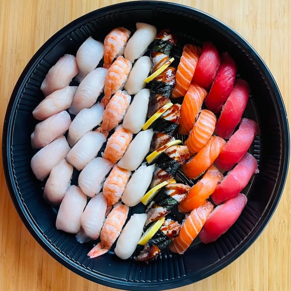 A large black platter filled with various Awi Sushi nigiri, including salmon, tuna, shrimp, and eel.