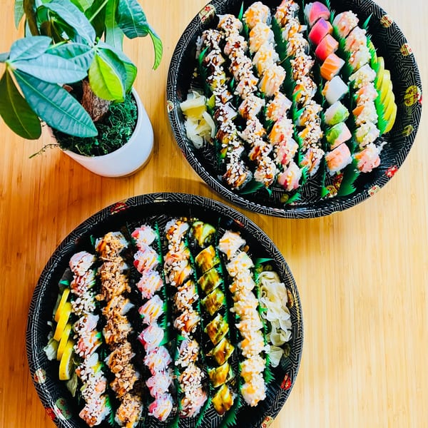 Two large platters of assorted Awi Sushi rolls, including colorful and fried varieties, on a wooden table.